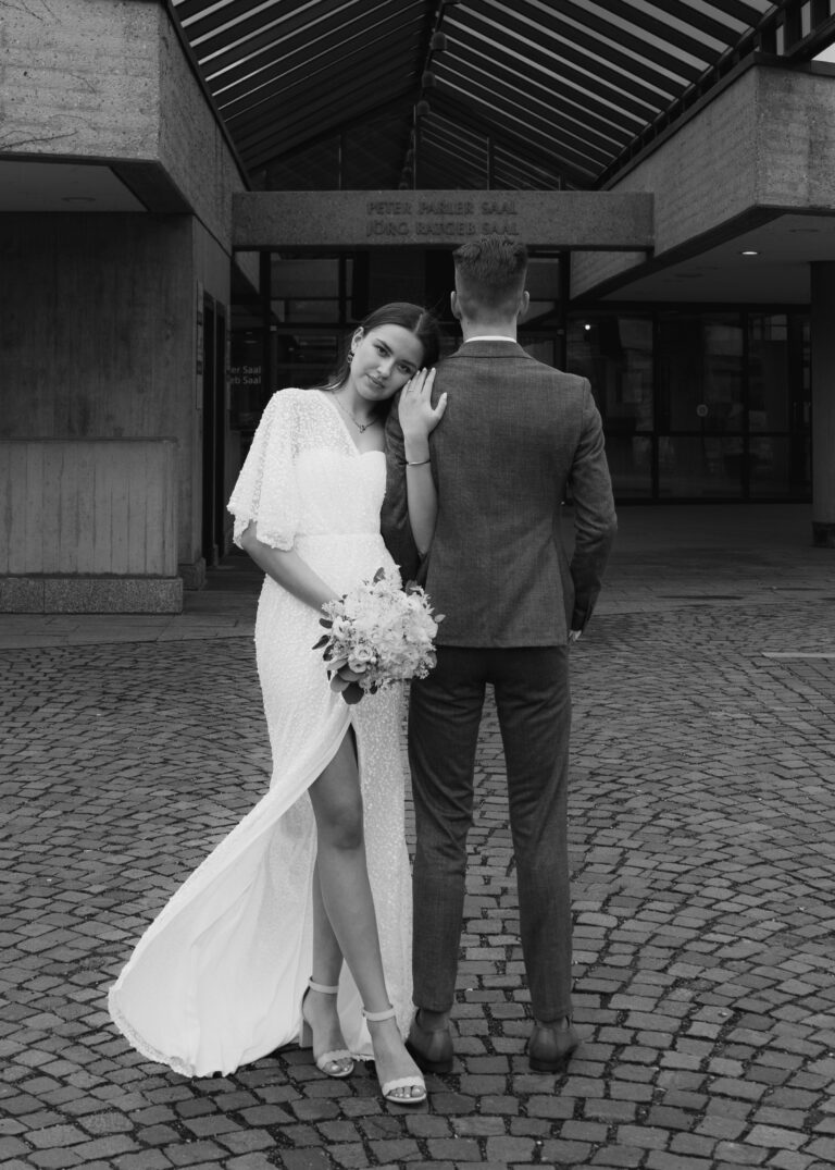 Braut hält einen Blumenstrauß in ihrer Hand und lehnt sich an die Schulter ihres Partners