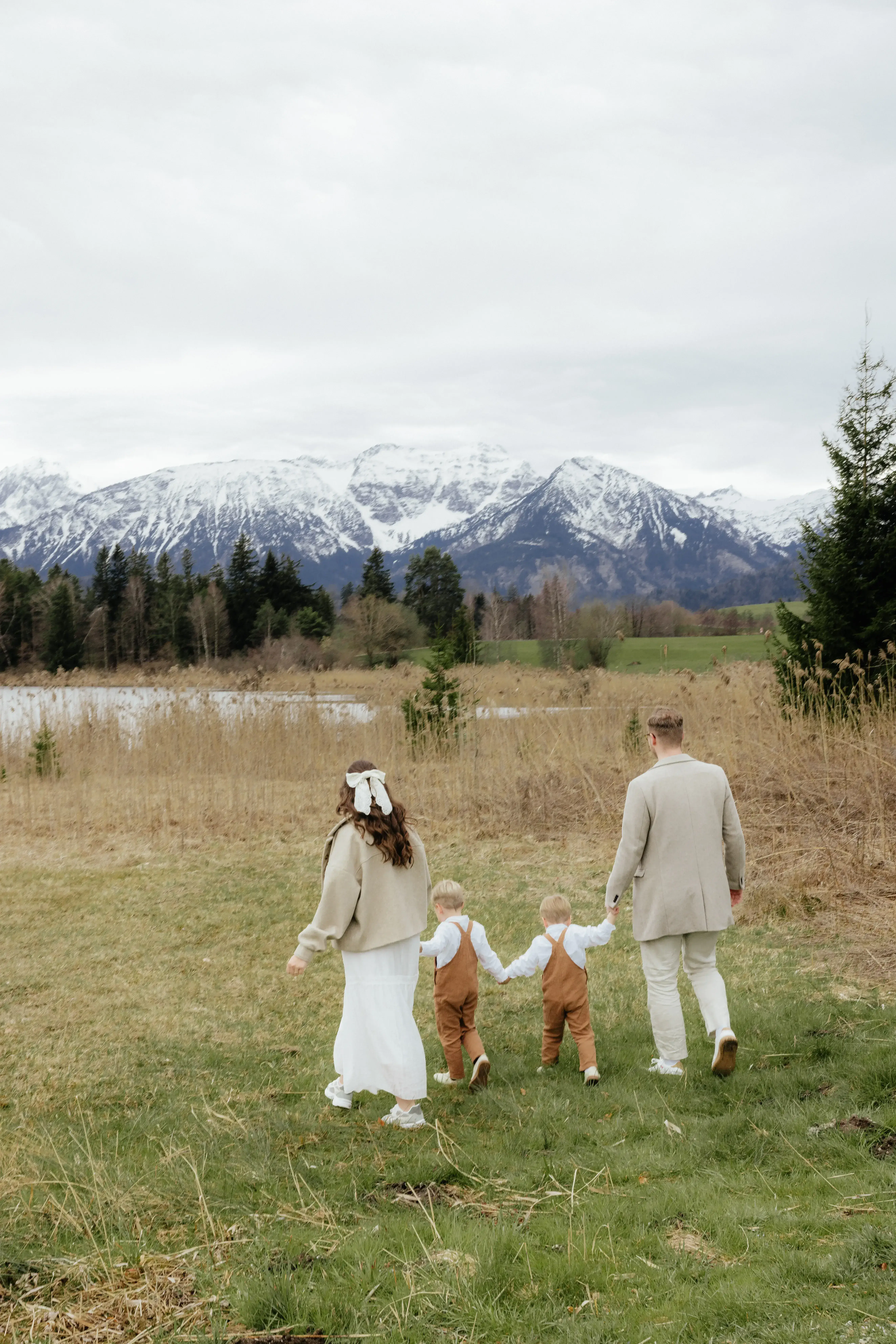Familie läuft Hand in Hand über Feld vor den Bergen in Füssen